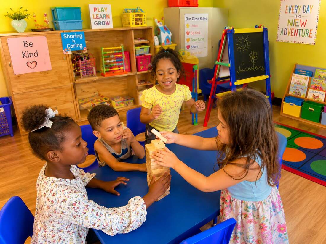 Three preschoolers painting and creating art together at a wood table in a bright studio classroom at Mercy Land Academy