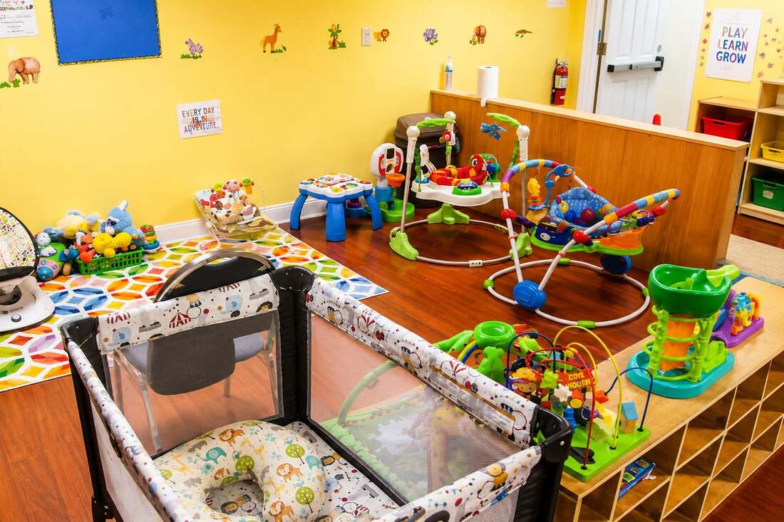 A caregiver tenderly holding and smiling at an infant in a calm, minimalist nursery at Mercy Land Academy